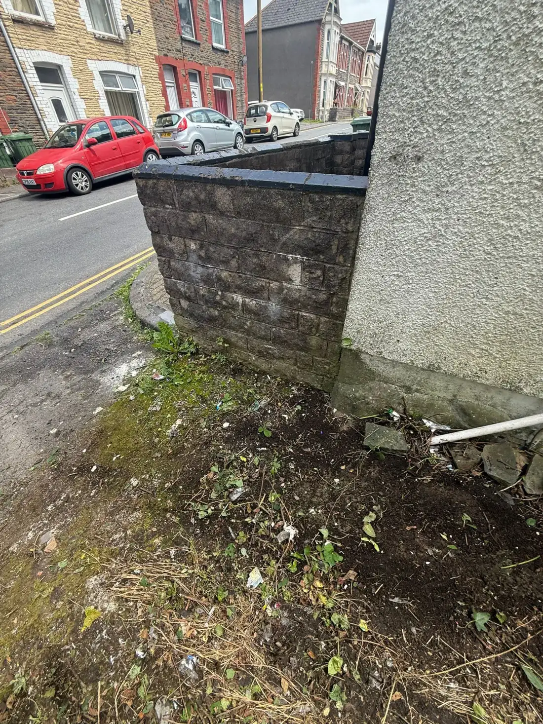 Bare soil and debris beside a garden wall