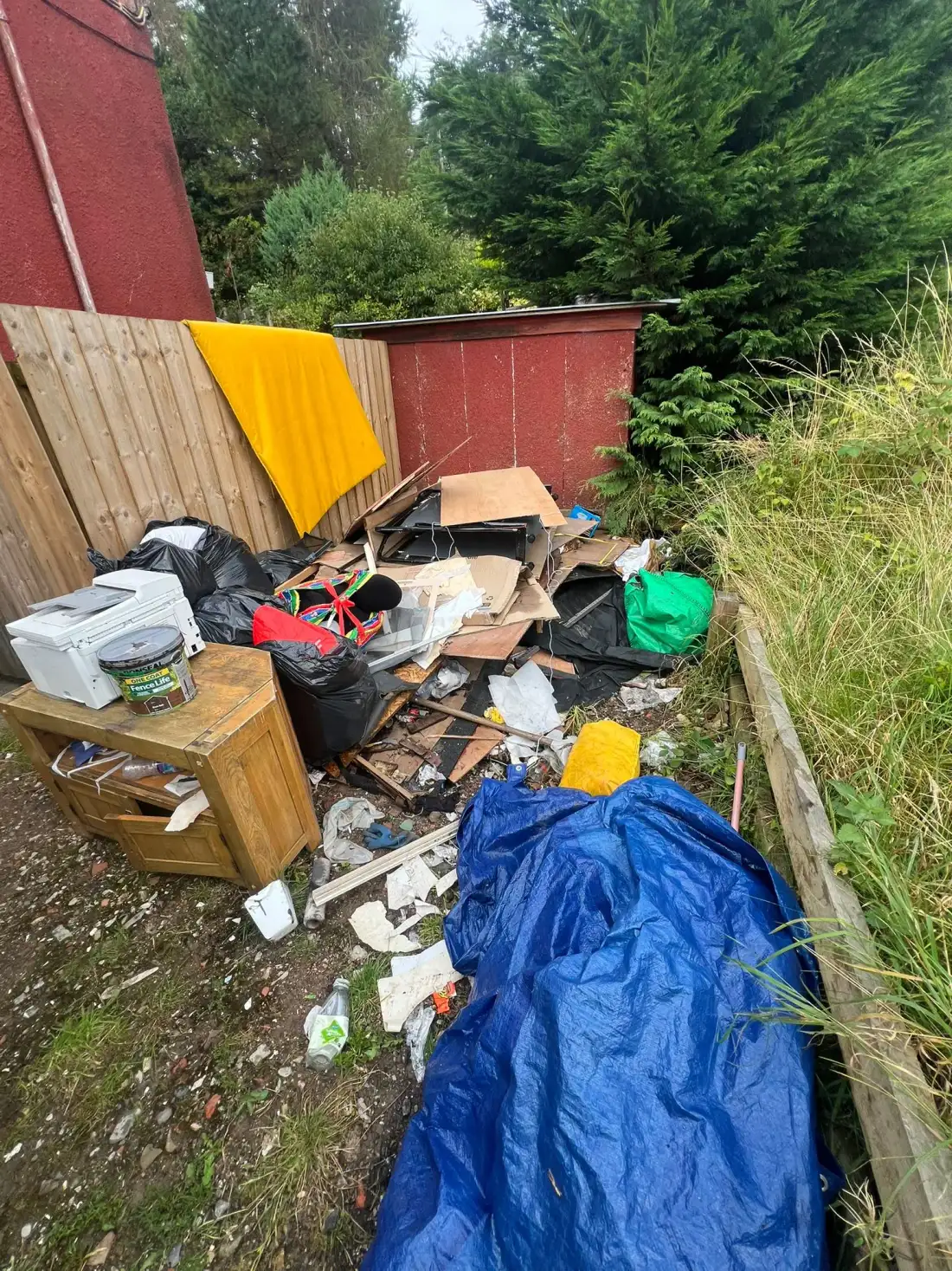 Old furniture, rubbish bags and a tarpaulin left beside a garden shed