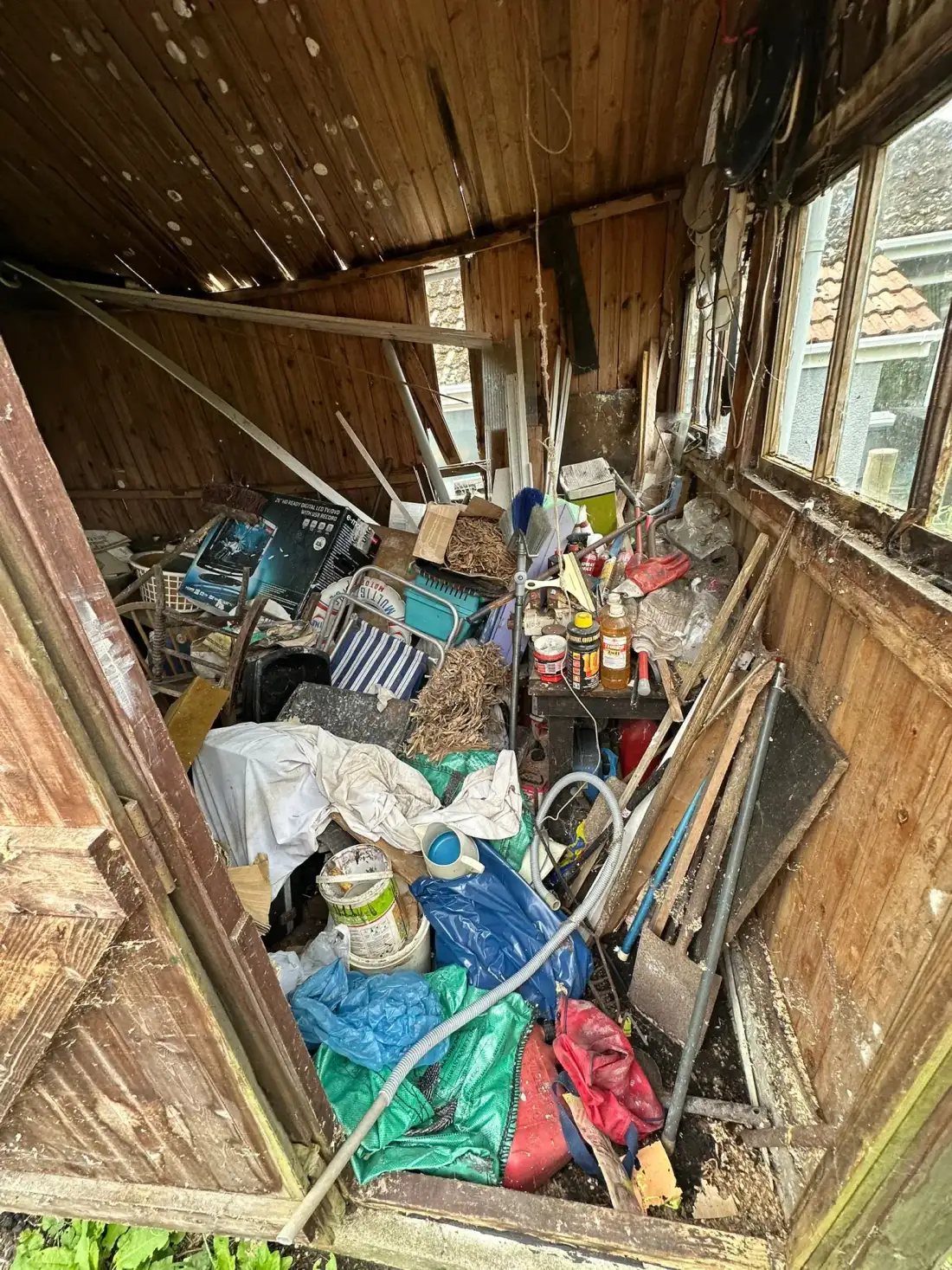 Timber shed packed with old tools, paint tins and tarpaulins