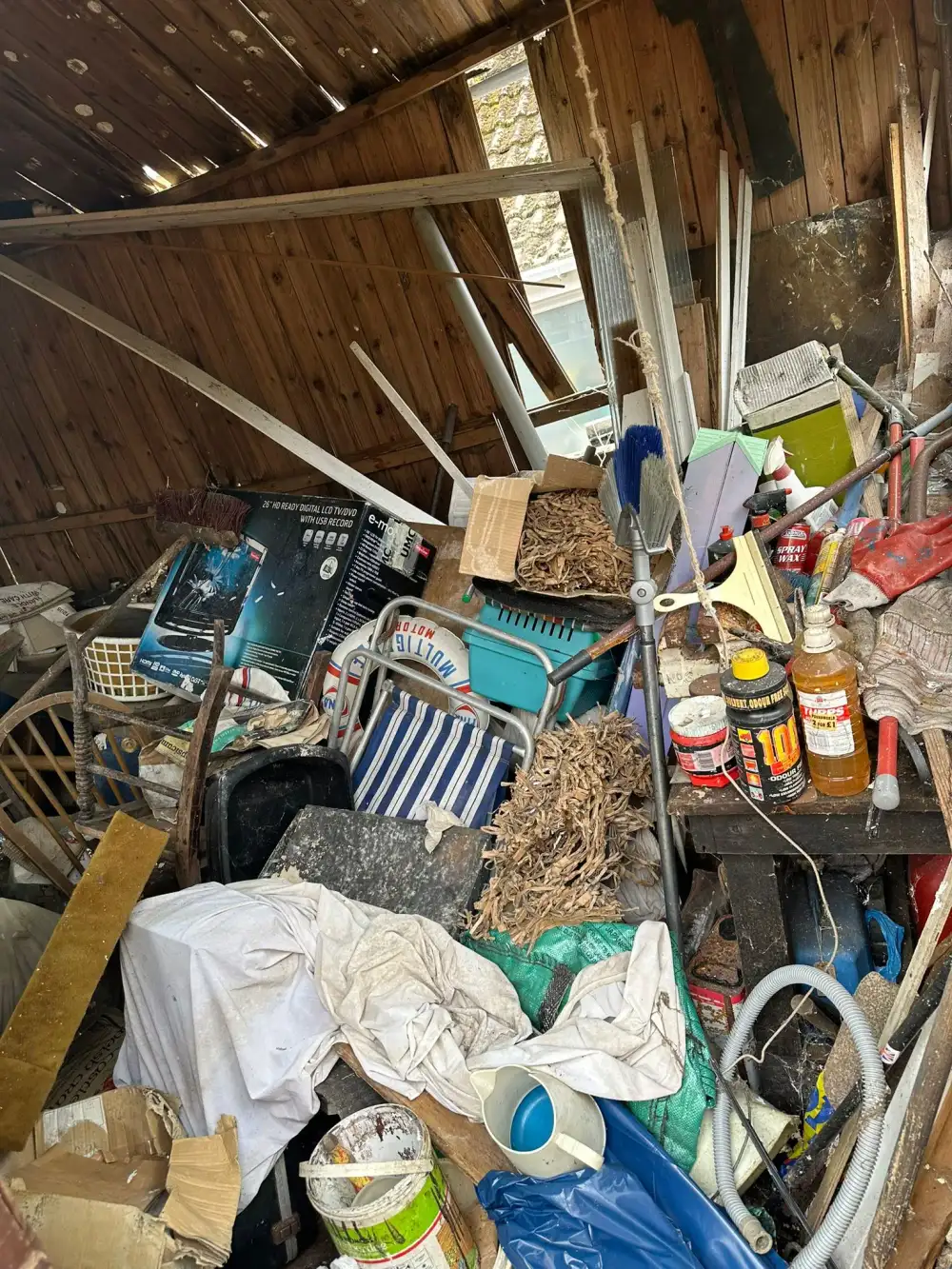 Timber shed overflowing with tools, paint tins and stored items